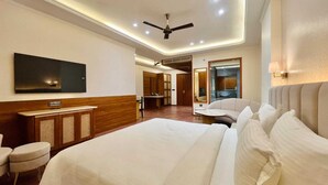 Una moderna camera d'albergo con un letto grande, una TV a schermo piatto, una ventola a soffitto e un'area salotto con divano e poltrone.