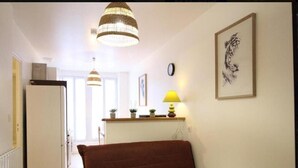 Un salón acogedor con un sofá marrón, una mesa de centro de madera, una lámpara colgante, una obra de arte enmarcada y una cocina visible al fondo.