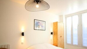 Un dormitorio con una cama grande, un armario de madera, una silla de mimbre y una lámpara fijada a la pared.