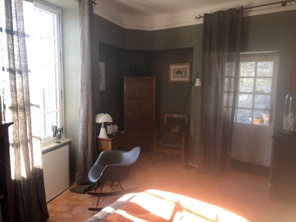A room with a bed, a rocking chair, a desk, a dresser, and a window with curtains.
