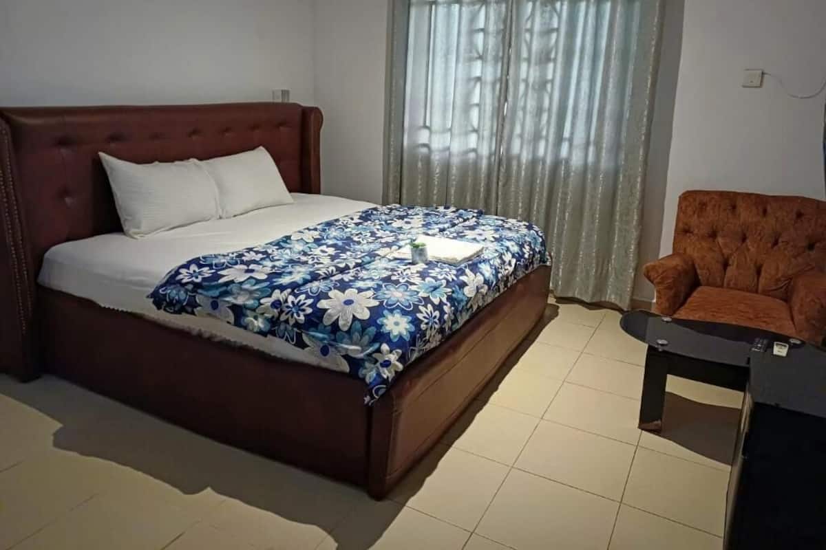 A bedroom with a bed, a chair, and a window with curtains.