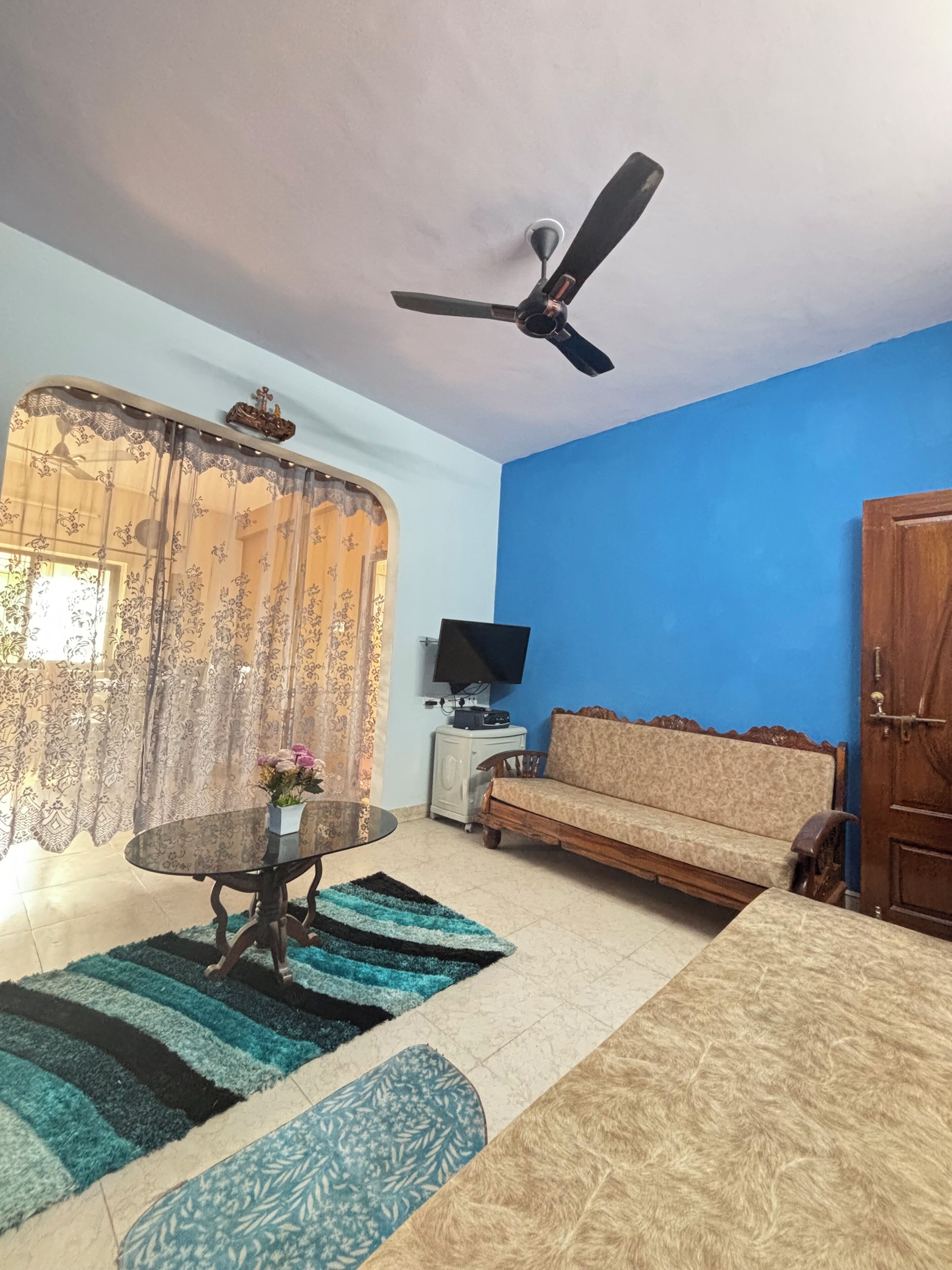 A living room with a blue wall, a ceiling fan, a sofa, a TV, and a table with a vase of flowers.