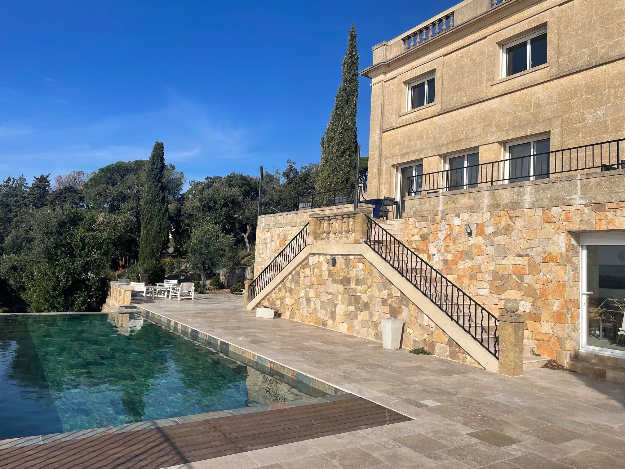 Un edificio de piedra con piscina, asientos al aire libre y una escalera que lleva a un balcón.
