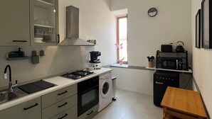 A compact kitchen with a gas stove, oven, microwave, and washing machine. There is a wooden table and a window with a view. - Penthouse23 Vatican Charming Apartment (Roma)