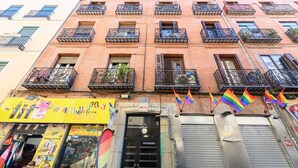 Un edificio de varios pisos con balcones, una tienda con letreros coloridos y banderas arcoíris.