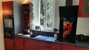 A kitchen with red cabinets, a black refrigerator, a double oven, and a window with a view of greenery.