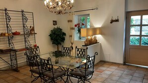 A dining area with a glass table, metal chairs, a chandelier, a potted plant, and a window with curtains.