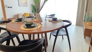 Uma área de refeições com uma mesa redonda, cadeiras pretas e um vaso com plantas verdes.
