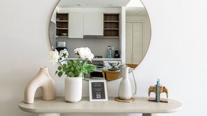 A modern kitchen with white cabinets, a round mirror, and a small table with decorative items. - 1BR Downtown and Dubai Frame Views (Dubai)