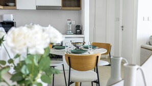 A modern dining area with a round table set for four, surrounded by wooden chairs. A vase with white flowers is in the foreground. - 1BR Downtown and Dubai Frame Views (Dubai)