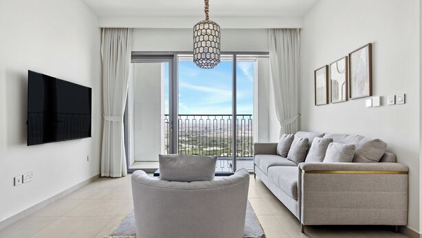 A modern living room with a grey sofa, a round armchair, and a flat-screen TV mounted on the wall. - 1BR Downtown and Dubai Frame Views (Dubai)