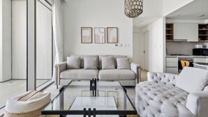 A modern living room with a sofa, a glass coffee table, and a tufted armchair. There is a kitchen visible in the background. - 1BR Downtown and Dubai Frame Views (Dubai)