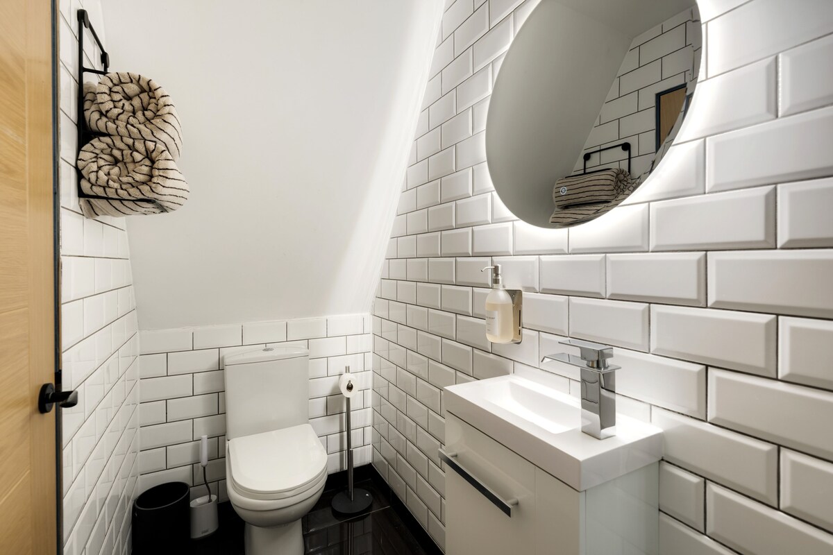 Un baño moderno con azulejos blancos tipo metro, un espejo redondo, un inodoro blanco y un lavamanos con grifo cromado.