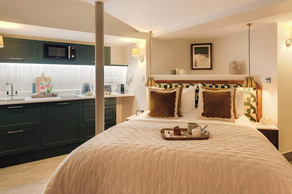 A hotel room with a bed, a bedside table with a tray of food, a microwave, a sink, and a green kitchen area.