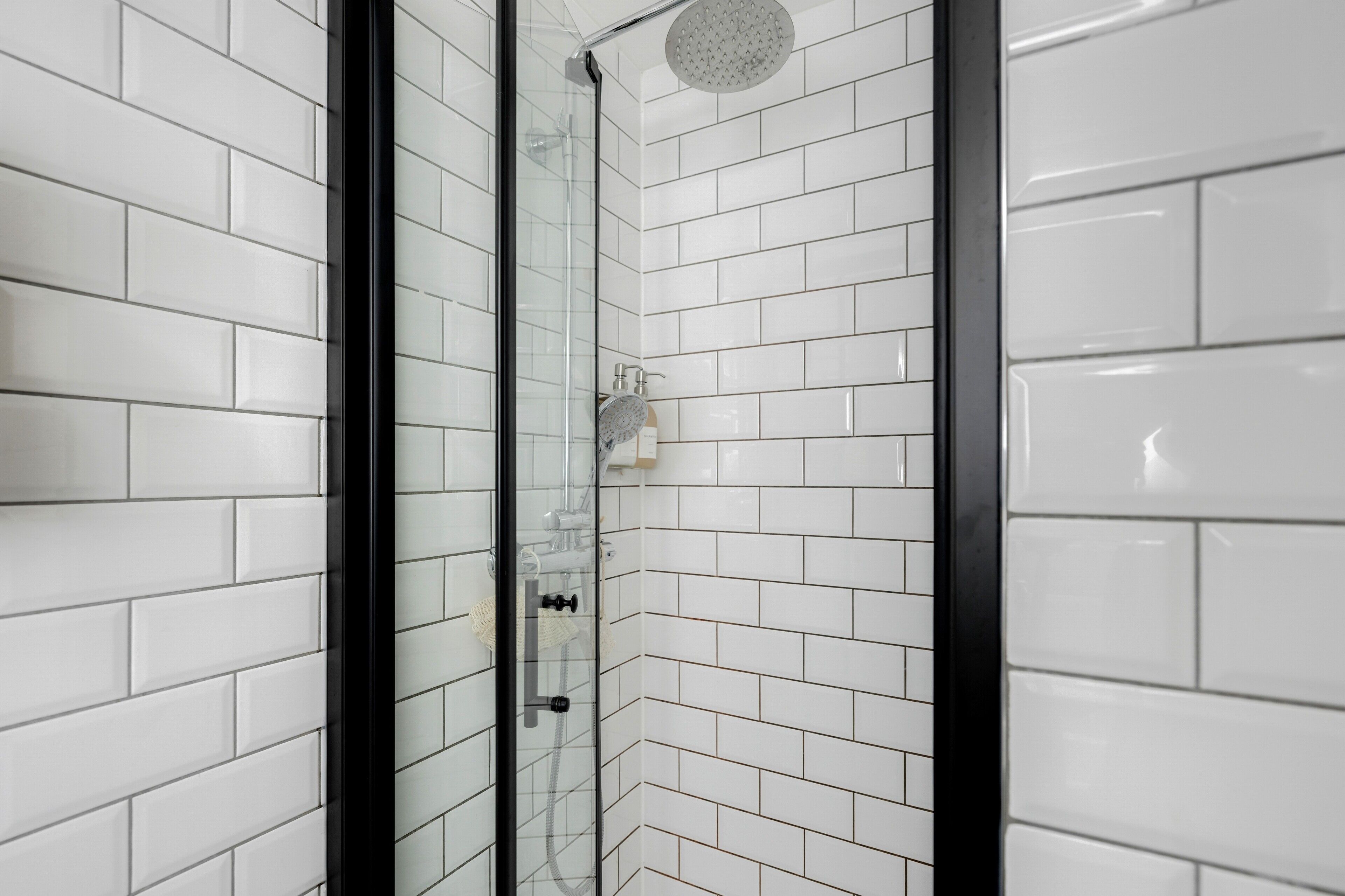 A modern bathroom with white subway tiles, a glass-enclosed shower, and a visible showerhead.