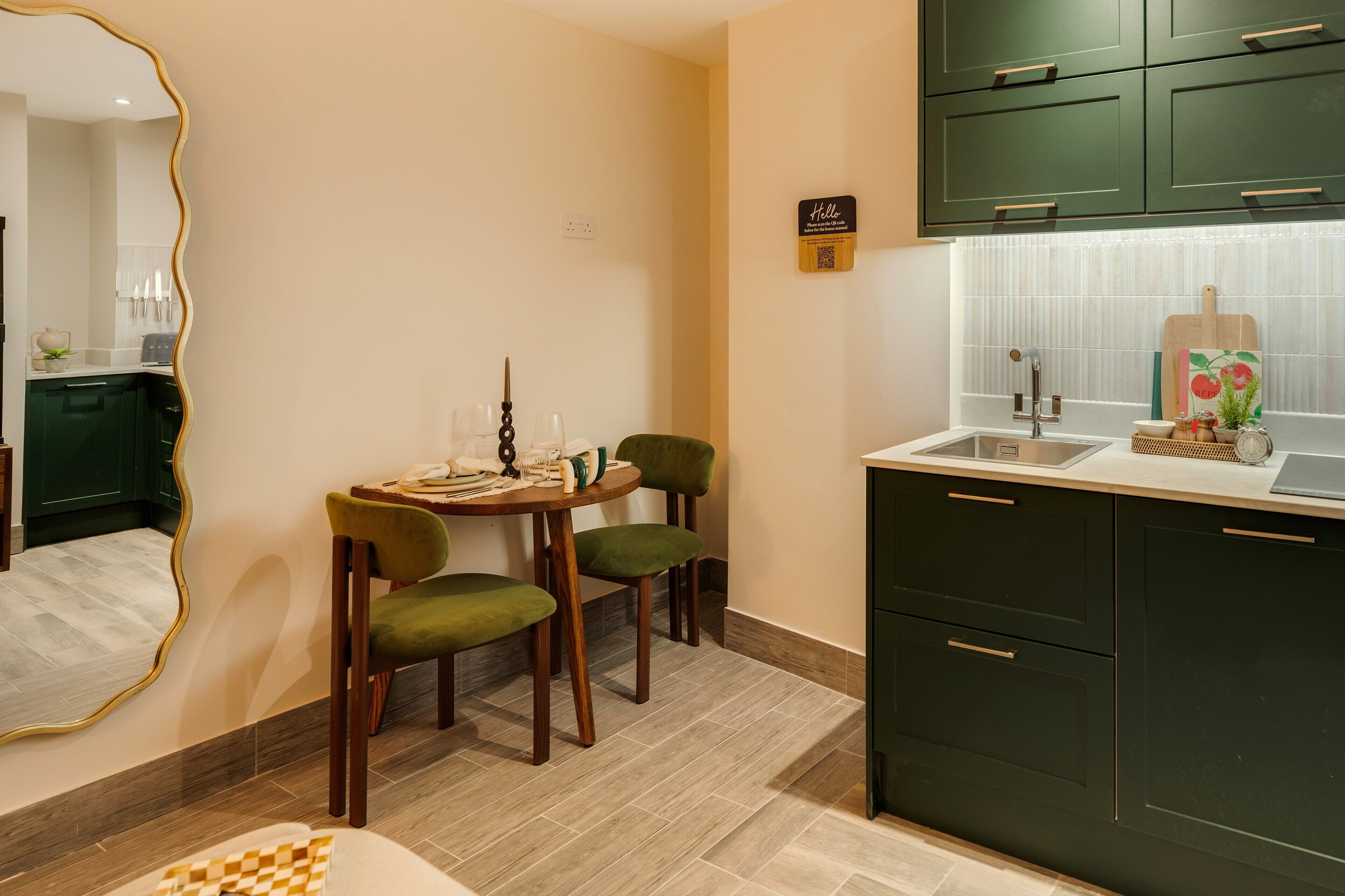 A compact kitchen with dark green cabinets, a white countertop, and a small dining area with two chairs and a table.