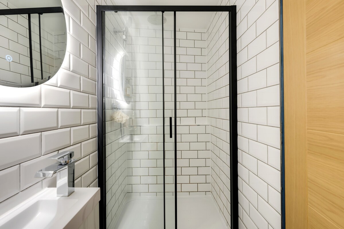 A modern bathroom with white subway tiles, a glass shower enclosure, and a wooden door.