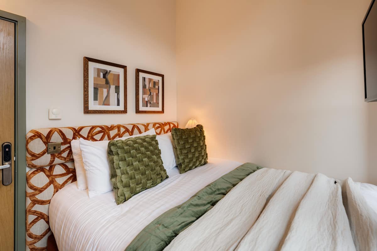 A neatly made bed with a patterned headboard, two framed artworks on the wall, and a bedside lamp.