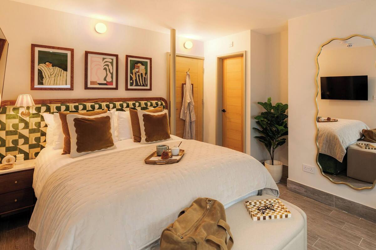A hotel room with a large bed, a TV, a mirror, and artwork on the wall.
