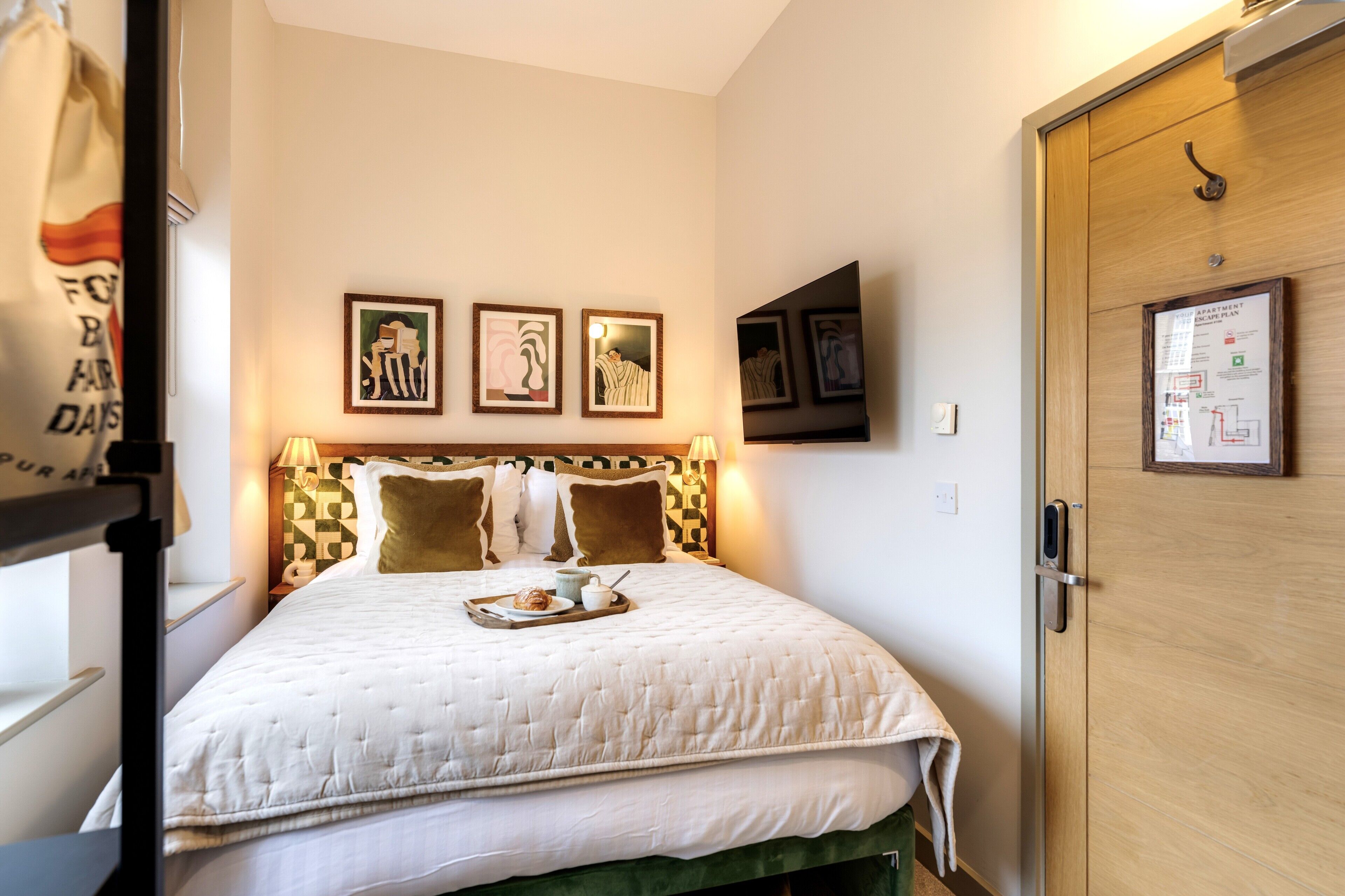 A neatly made bed with a quilt, pillows, and a tray with a cup and a pastry. There are framed pictures on the wall above the bed.