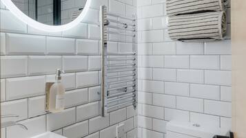 Un baño moderno con azulejos blancos tipo metro, un espejo redondo con luz, un perchero, un inodoro y un dispensador de jabón para manos.