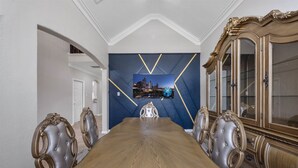 A dining room with a long wooden table, ornate chairs, a large cabinet, and a cityscape painting on the wall.