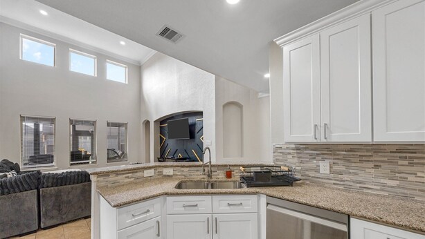A modern kitchen with white cabinets, a granite countertop, and a built-in oven.