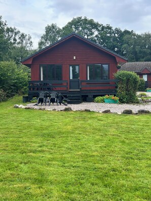A red wooden cabin with a porch, a small table, and chairs.