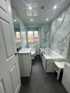 A modern bathroom with a marble wall, a bathtub, a sink, and a toilet.