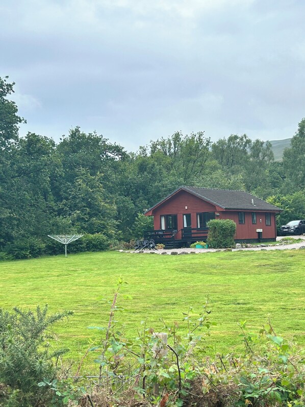 A red house with a sloped roof, surrounded by a grassy field and dense trees.