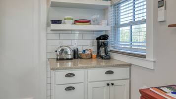 A kitchen with white cabinets, a granite countertop, a coffee maker, and a window with blinds.