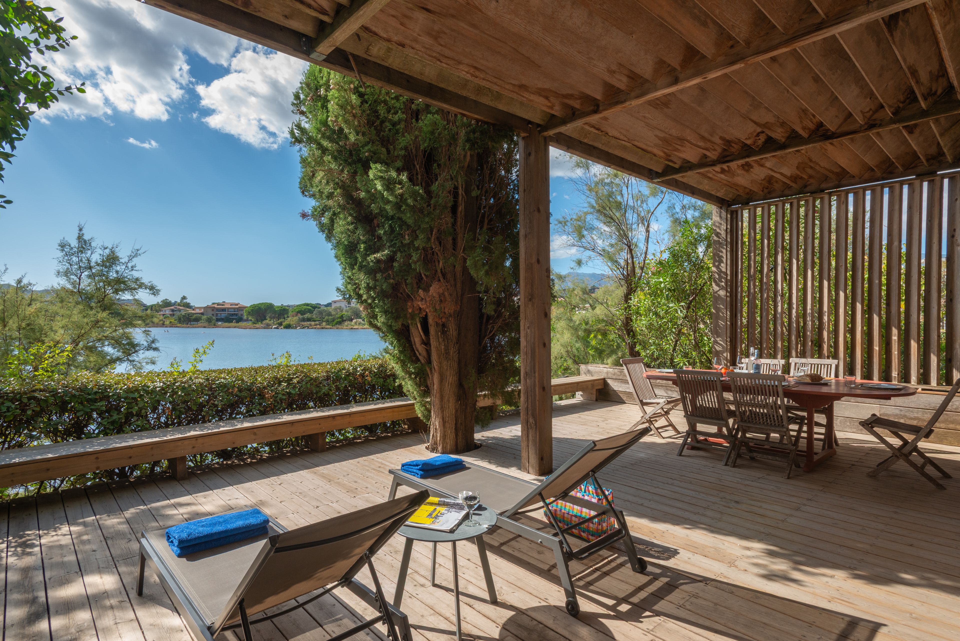 Una terraza de madera con una mesa y sillas, con vista a un cuerpo de agua.