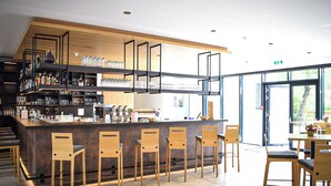 Uma área de bar moderna com cadeiras de madeira, balcão e prateleiras repletas de garrafas e copos.