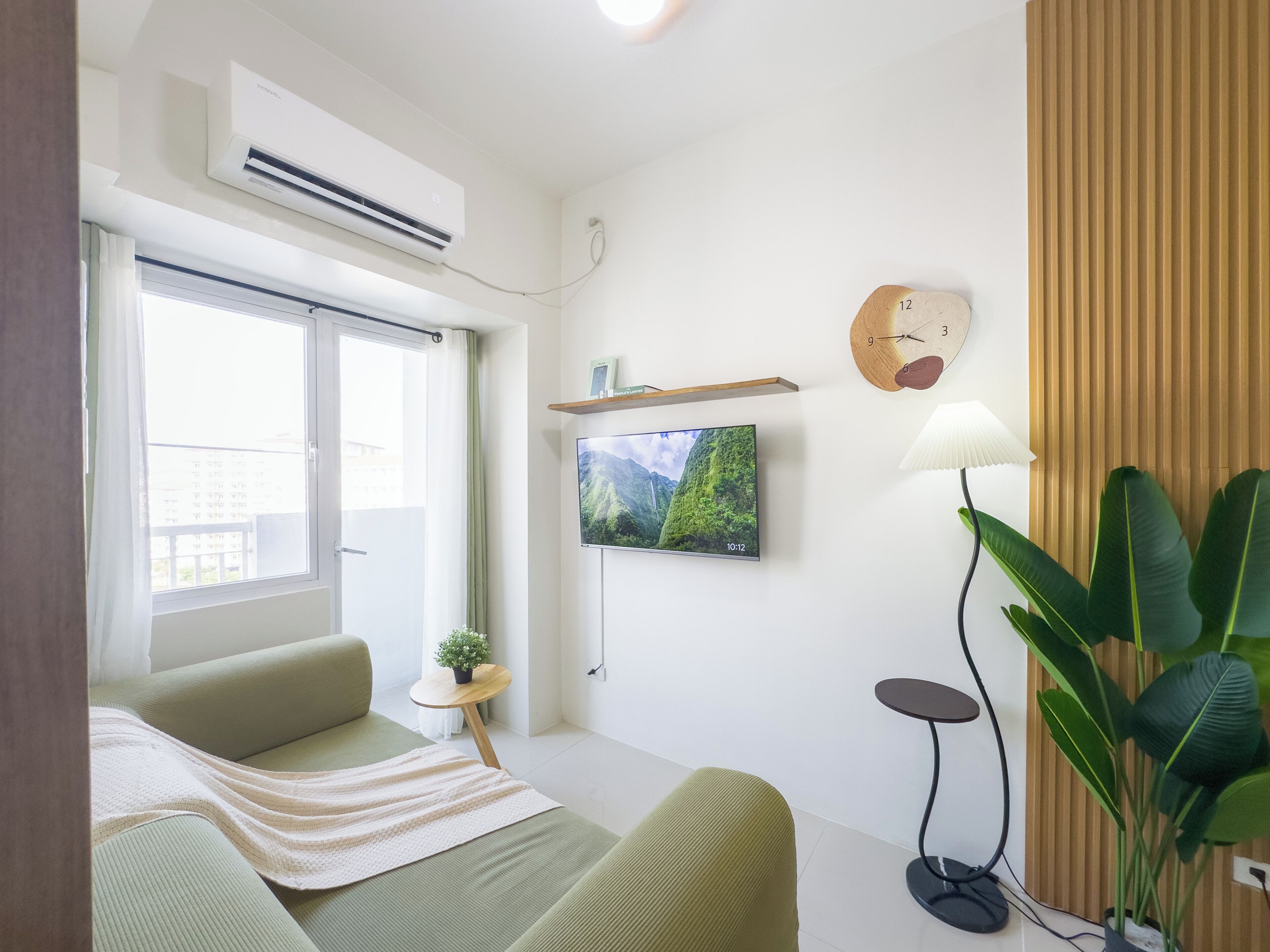 Una sala de estar moderna con un sofá, un televisor montado en la pared, una mesita con una planta y un ventanal grande.