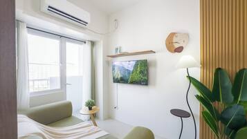 Una sala de estar moderna con un sofá, un televisor montado en la pared, una mesita con una planta y un ventanal grande.