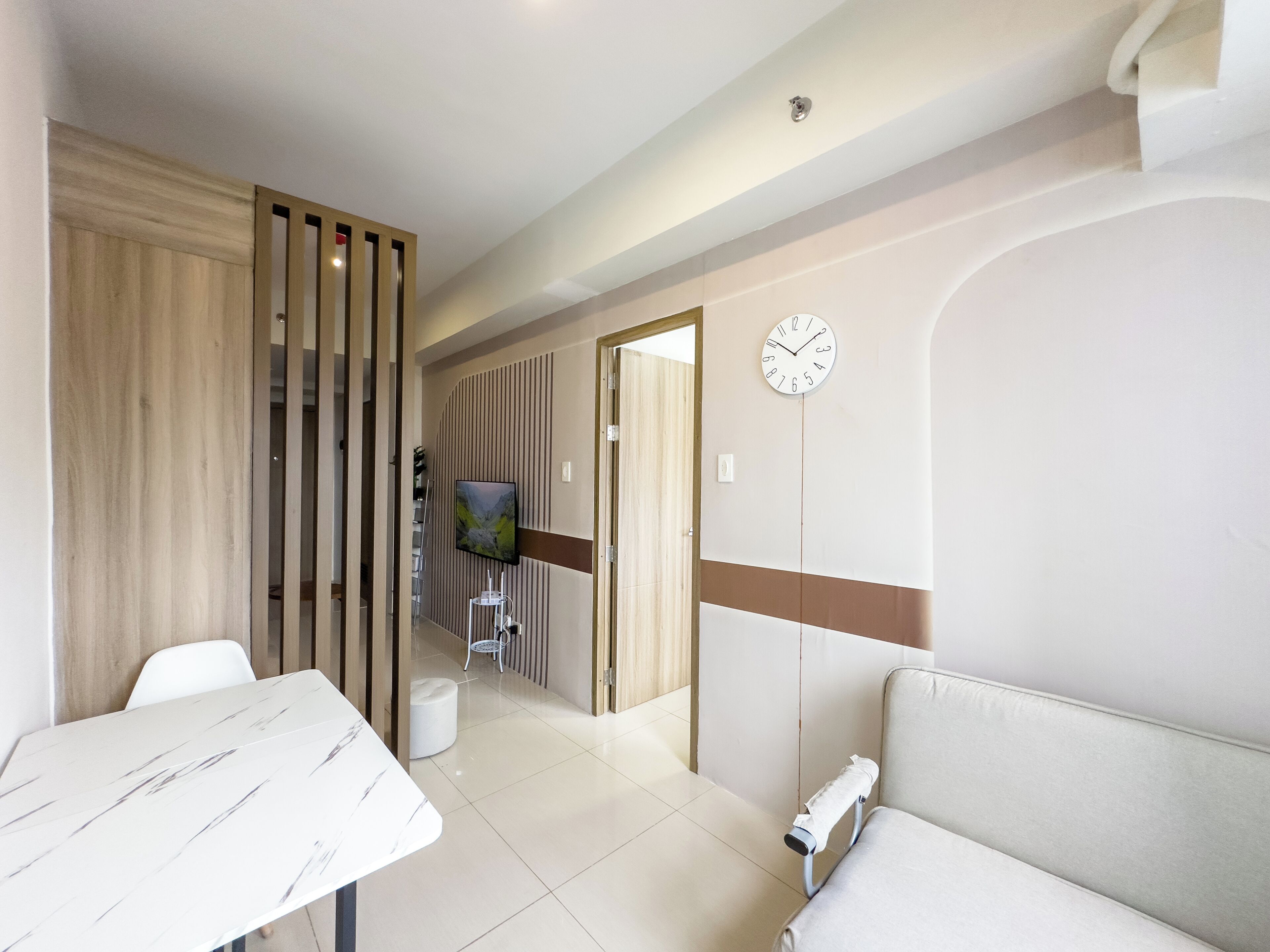 A modern hotel room with a white marble table, a cushioned sofa, a TV mounted on the wall, and a wooden partition.