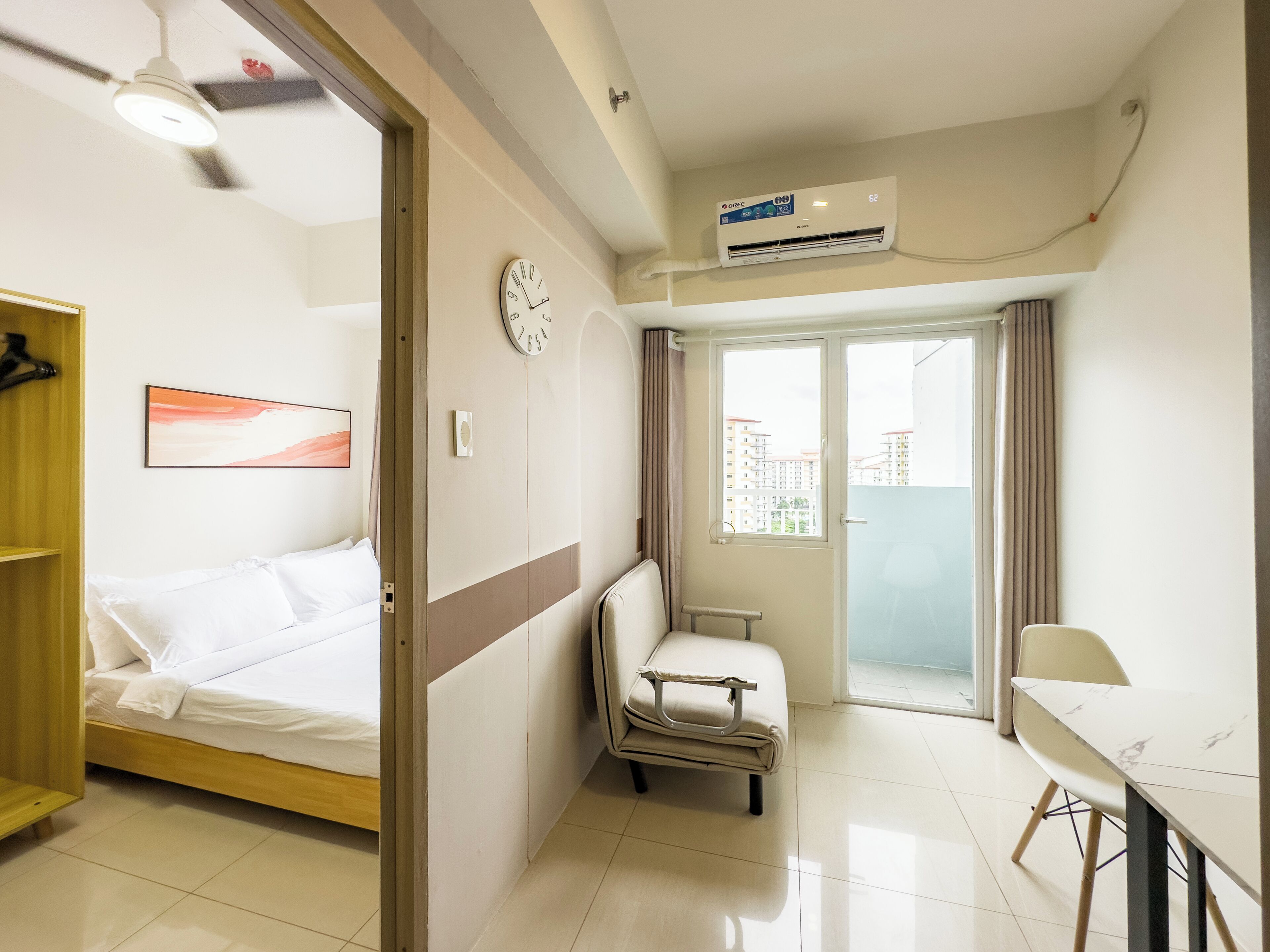 Una camera d'albergo con un letto, una sedia, un tavolo, una sveglia e un condizionatore d'aria.