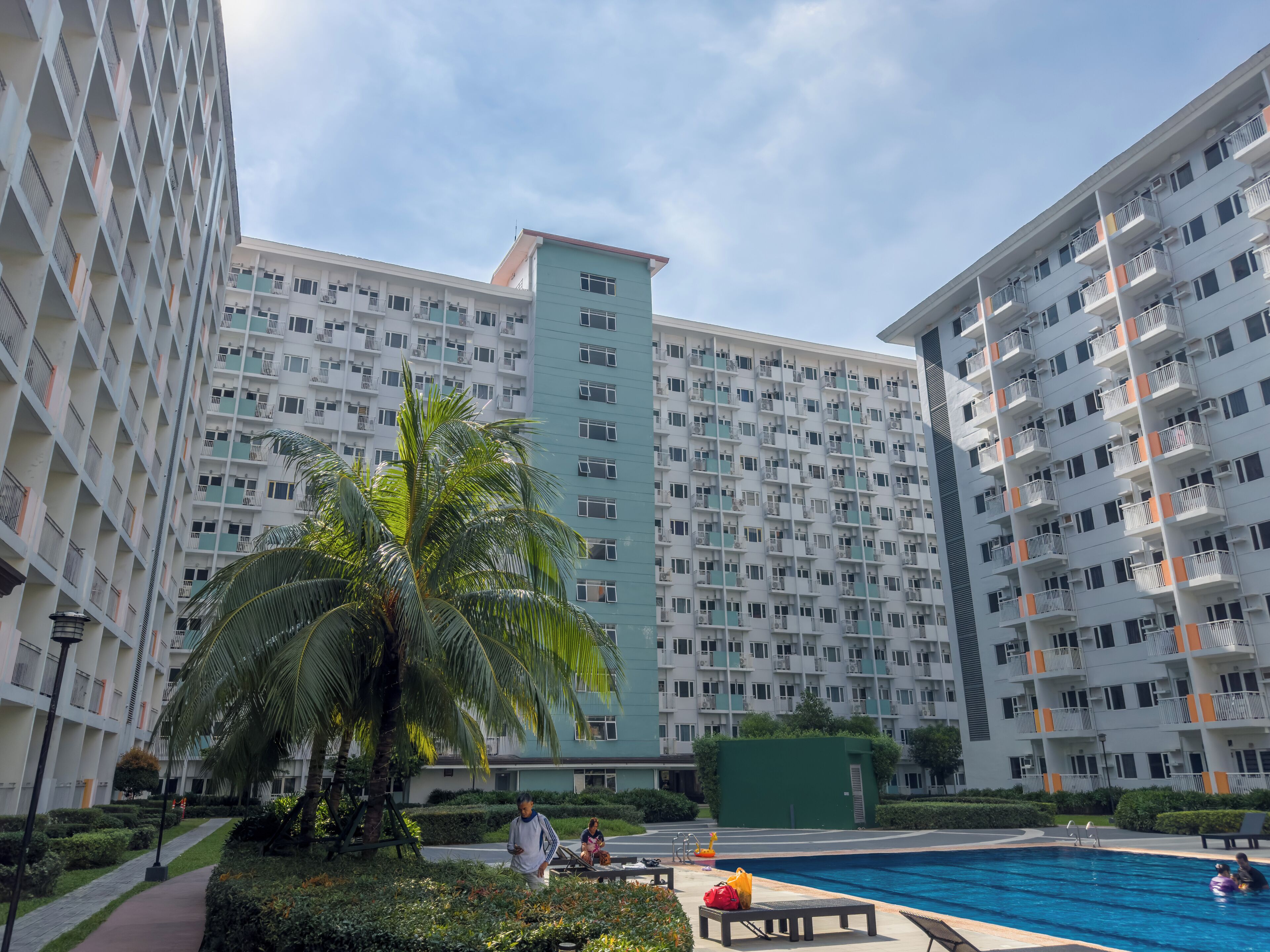A modern apartment building with multiple balconies, a swimming pool, and well-maintained greenery.