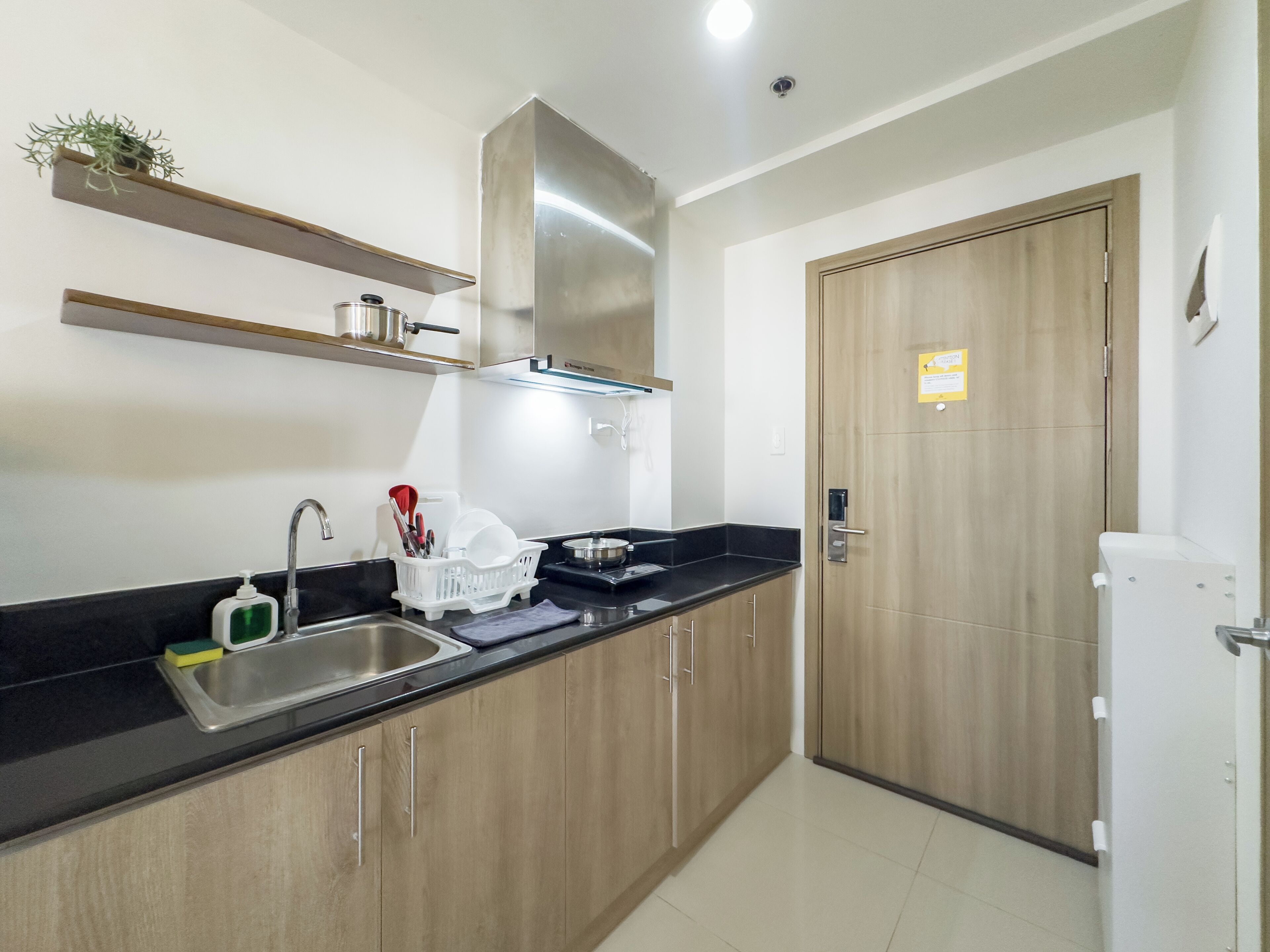 A kitchen with a sink, wooden cabinets, a stainless steel range hood, and a white refrigerator.