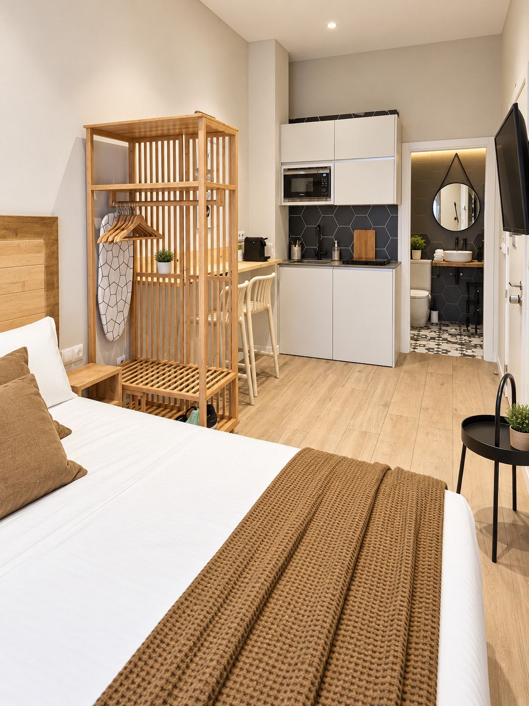 Une chambre d’hôtel moderne équipée d’un lit, d’une armoire en bois, d’une kitchenette et d’une salle de bain.