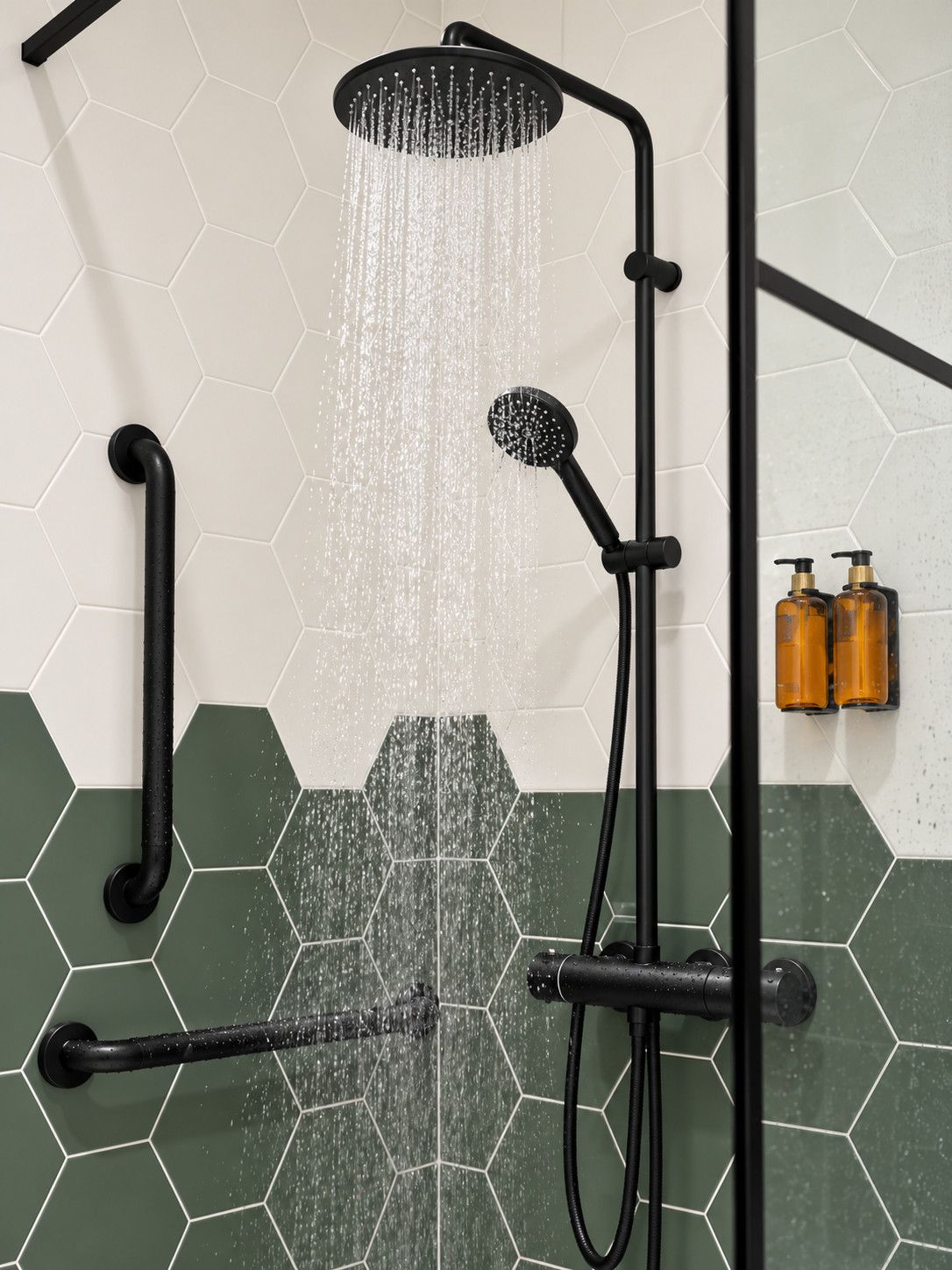 Une douche dotée de plusieurs jets et d’un pommeau de douche à main, installée sur un mur recouvert de carreaux hexagonaux de deux couleurs différentes.