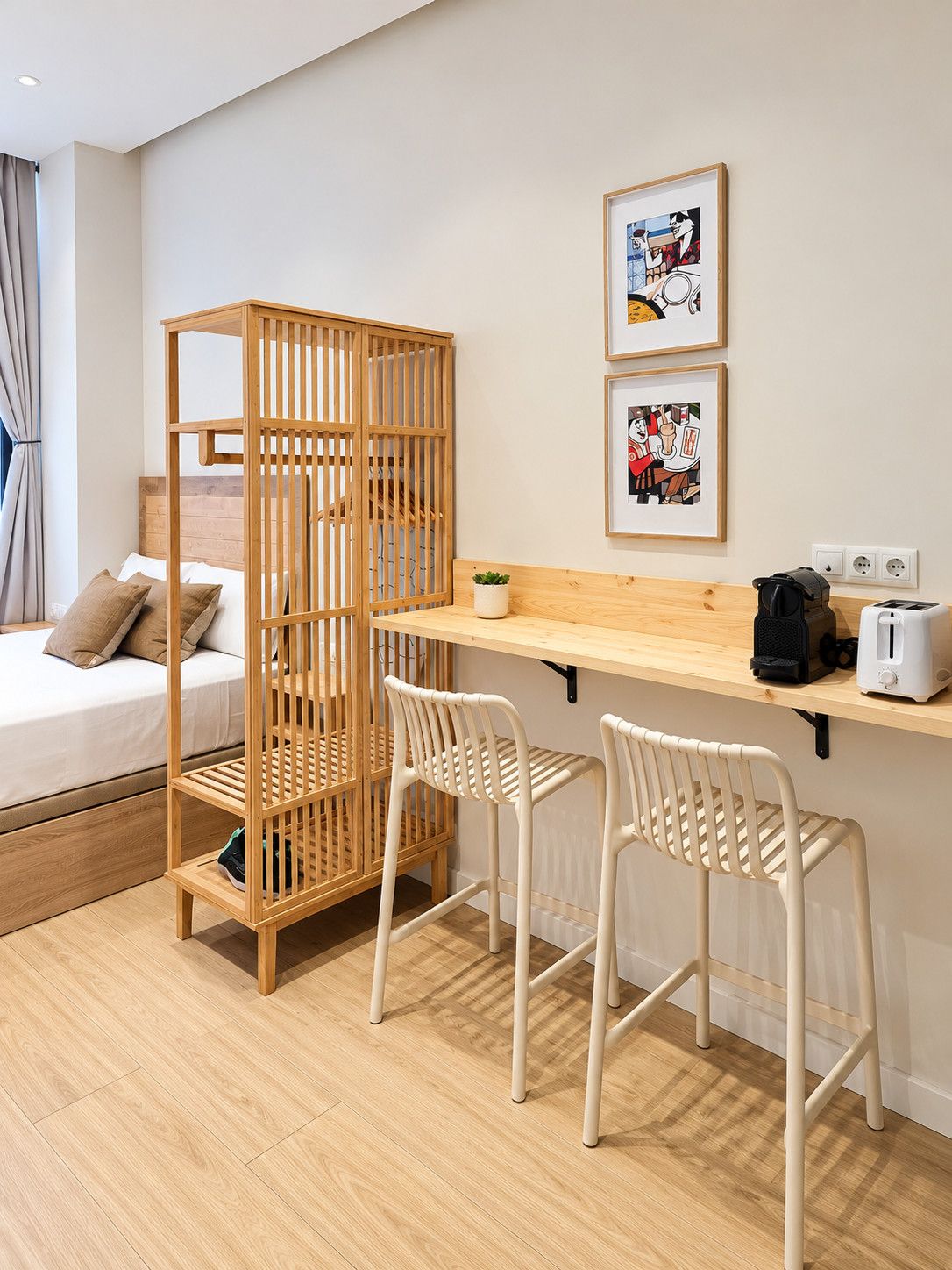 A room with a bed, a wooden partition, two white chairs, a wooden desk, a toaster, and two framed pictures on the wall.