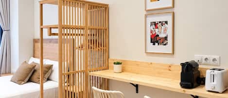 A room with a bed, a wooden partition, two white chairs, a wooden desk, a toaster, and two framed pictures on the wall.