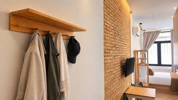 Een moderne kamer met een bakstenen muur, een houten plank met kleding, een aan de muur bevestigde televisie, een bed en een raam met gordijnen.