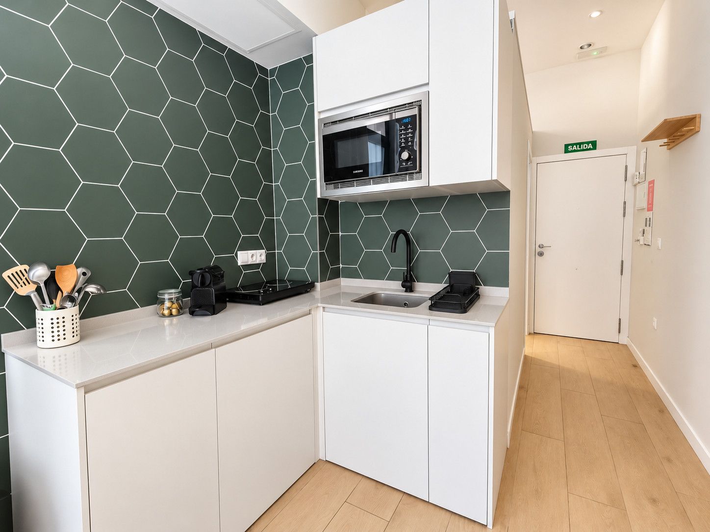 Een kleine keuken met witte kastjes, een magnetron en een spoelbak.