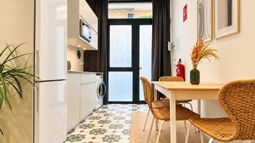 Een kleine keuken met een wasmachine, een eettafel met rieten stoelen en een vloer met een patroon.