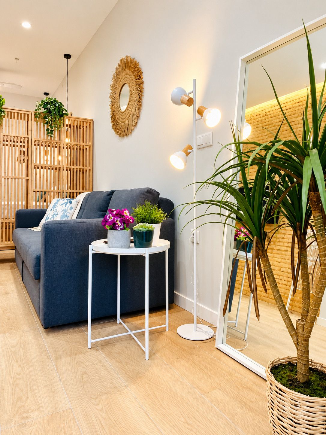 Een moderne woonkamer met een bank, een rond bijzettafeltje met planten, een spiegel en een houten scheidingswand.