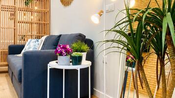 Een moderne woonkamer met een bank, een rond bijzettafeltje met planten, een spiegel en een houten scheidingswand.