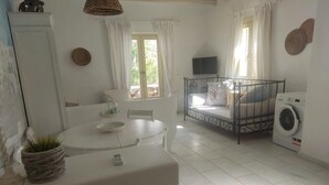 A clean, well-lit room with a bed, a washing machine, a dining table, and a TV. - THEROS CASA LOGARAS (Paros)