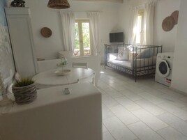 Una habitación limpia y bien iluminada con una cama, lavadora, mesa de comedor y televisor.